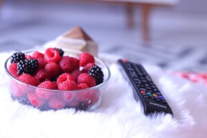 Persone che mangiano davanti alla TV, distratte e con cibo in mano, illustrando il tema dell'articolo.